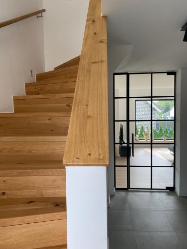 Holztreppe mit Geländer und Blick auf einen Glastürbereich mit Gartensicht.