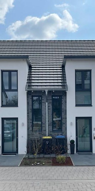 Zweifamilienhaus mit Fahrradständer und Mülltonnen im Vordergrund.