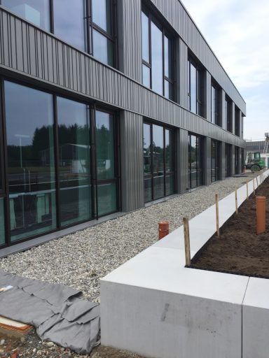 Moderne Gebäudefassade mit großen Fenstern und Schotterbereich daneben.