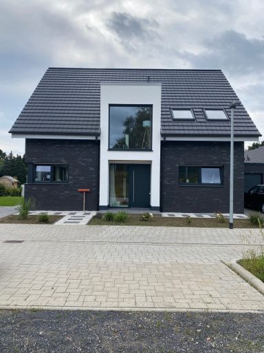 Modernes Haus mit schwarzer Fassade, großen Fenstern und einem stilvollen Satteldach.