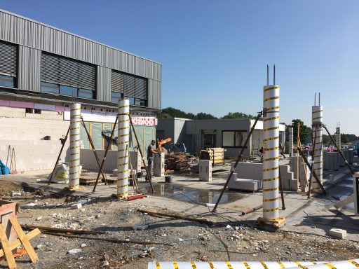 Bauplatz mit Betonstützen und Baustellenmaterialien unter klarem Himmel.