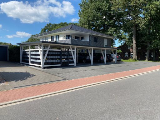 Zweistöckiges Haus mit überdachten Parkplätzen und Bäumen im Hintergrund.
