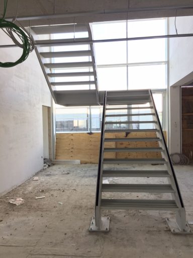 Moderne Treppe aus Stahl mit Glasfenster im Hintergrund und unvollendeter Umgebung.