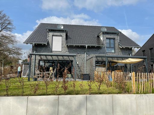 Modernes Haus mit Garten, Terrasse und Sonnenschutz, umgeben von Natur.