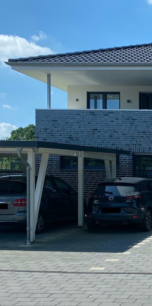 Zwei Autos stehen unter einem Carport vor einem modernen Gebäude.