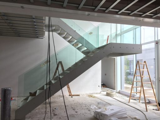 Moderne Treppe aus Beton und Glas in einem unfertigen Innenraum mit Baustellenmaterial.