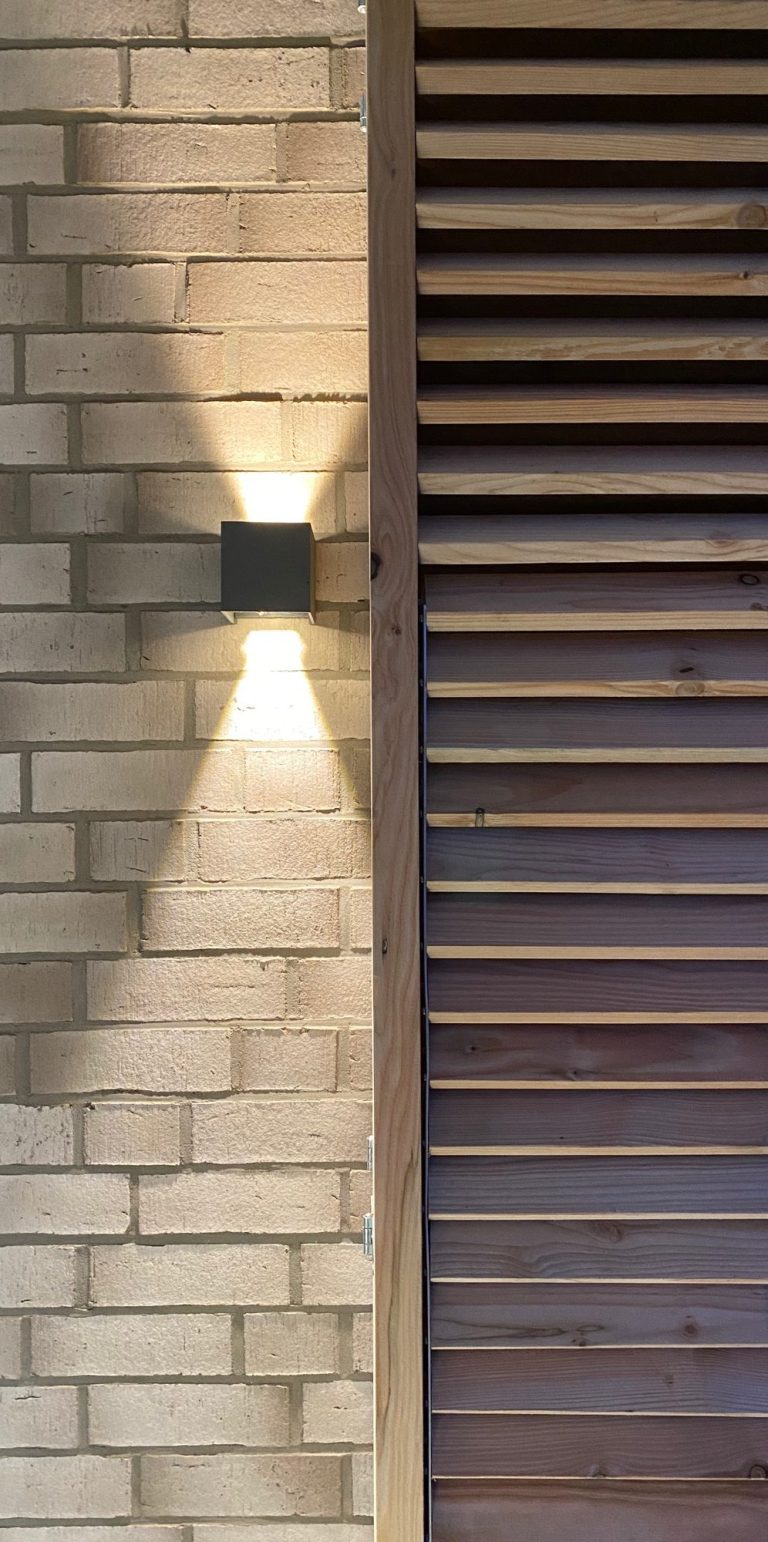 Wandleuchte wirft Schatten auf eine moderne Ziegelwand und Holzverkleidung.
