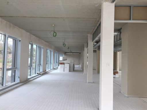 Leerer Raum mit großen Fenstern und Sicht auf eine unvollendete Bauarbeit.