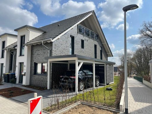 Moderne Doppelhaushälfte mit Carport und Garten, umgeben von Wolken am Himmel.