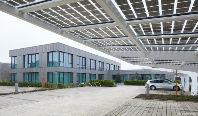 Moderne Bürogebäude mit überdachtem Parkplatz und Solarzellen im Vordergrund.