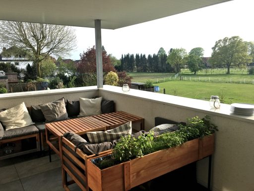 Hübscher Balkon mit Sitzgelegenheiten und Pflanzkübel, Blick auf eine grüne Wiese.
